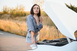 hermosa Delgado niña en camisa y pantalones cortos mira en abierto coche capucha en un la carretera foto