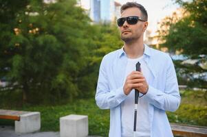 Young handsome blinded man walking with stick in town photo