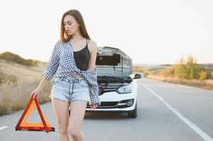 Beautiful sexy woman holding an emergency stop sign near a broken car. photo