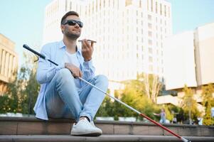 joven ciego hombre con teléfono inteligente en ciudad, vocación foto