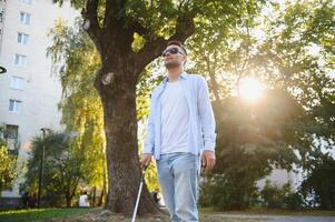 joven hermoso cegado hombre caminando con palo en pueblo foto