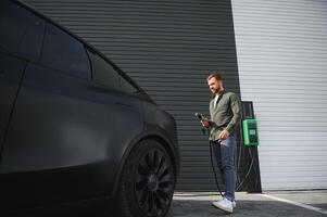 A man stands near a charging station and charges his electric car photo