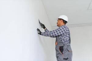 un indio trabajador trabajos en un vacío departamento. un hombre en un uniforme hace refacción dentro el edificio foto