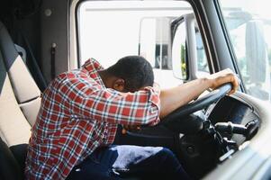 cansado de trabajar. sentado en el cabina. joven africano americano camión conductor es con su vehículo a tiempo de día. foto