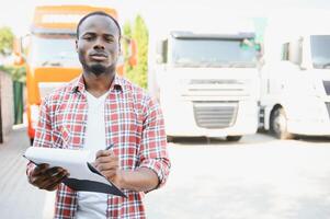 Front view. Young african truck driver is with his vehicle at daytime. photo