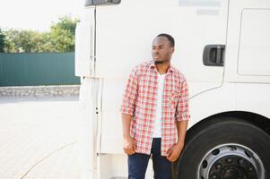 Front view. Young african truck driver is with his vehicle at daytime. photo