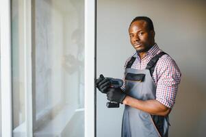 joven africano personal de mantenimiento en uniforme fijación vaso ventana con destornillador foto