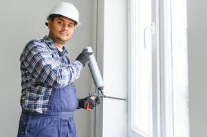 indio trabajador utilizando un silicona tubo para reparando de ventana interior foto