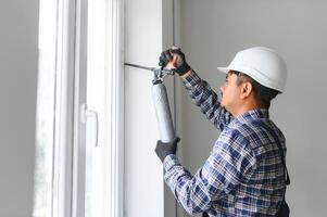 indio trabajador utilizando un silicona tubo para reparando de ventana interior foto