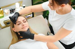 proceso de creando permanente frente maquillaje con un máquina a belleza salón foto