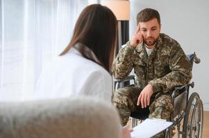 Depressed guy in camouflage uniform paralyzed soldier in wheelchair visiting female psychologist. photo