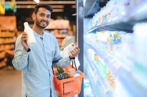 Portrait of handsome young Indian man standing at grocery shop or supermarket, Closeup. Selective Focus. photo