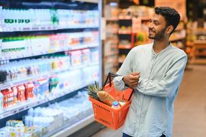 Portrait of handsome young Indian man standing at grocery shop or supermarket, Closeup. Selective Focus. photo