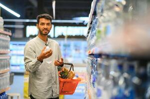 Portrait of handsome young Indian man standing at grocery shop or supermarket, Closeup. Selective Focus. photo