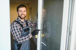 Workman in overalls installing or adjusting plastic windows in the living room at home photo