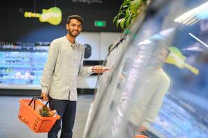 Portrait of handsome young Indian man standing at grocery shop or supermarket, Closeup. Selective Focus. photo