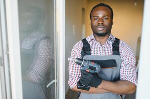 Young African Repairman In Overalls Installing Window photo