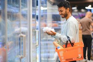 Portrait of handsome young Indian man standing at grocery shop or supermarket, Closeup. Selective Focus. photo