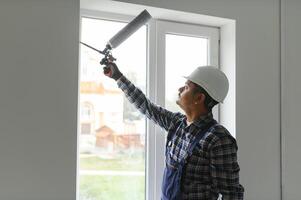 indio trabajador utilizando un silicona tubo para reparando de ventana interior foto