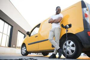 africano hombre participación cargar cable en en mano en pie cerca lujo eléctrico coche foto