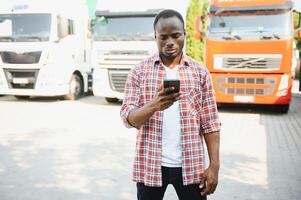 Front view. Young african truck driver is with his vehicle at daytime. photo