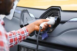 african man holding charge cable in on hand standing near electric car. photo