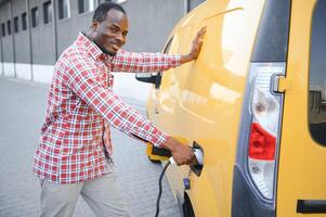 elegante hombre inserta el cargando cable dentro el enchufe de eléctrico coche foto