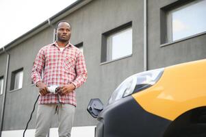 Stylish man inserts the charging cable into the socket of electric car photo