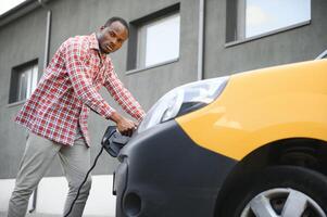 elegante hombre inserta el cargando cable dentro el enchufe de eléctrico coche foto