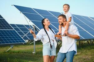 joven familia de Tres es agachado cerca fotovoltaica solar panel, pequeño chico y padres. moderno familia concepto. el concepto de verde energía foto