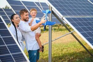 joven familia con un pequeño niño en su brazos en un antecedentes de solar paneles un hombre y un mujer Mira a cada otro con amor. solar energía concepto. foto