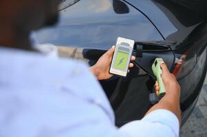 hombre enchufar en eléctrico coche fuera de oficina en coche parque cargando foto