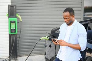 hombre enchufar en eléctrico coche fuera de oficina en coche parque cargando foto