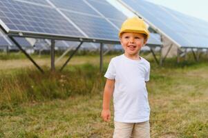 Portrait of a child near the solar panels. A little boy in a protective helmet near solar panels with his hand. Shooting at a solar power plant. Ecological farm. Solar power station. People photo