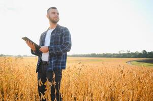 Young agronomist holds tablet touch pad computer in the soy field and examining crops before harvesting. Agribusiness concept. agricultural engineer standing in a soy field with a tablet. photo