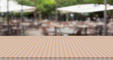 empty gingham pattern table top with blurry outdoor restaurant or cafe background, blank counter for product montage advertising photo