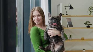 Happy young woman hugs her dog at home standing near the window video