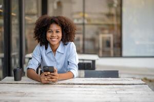 black business woman sitting With a coffee mug and a phone in her hand, She sat there smiling and looking straight into the camera. photo