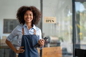 Successful african american woman in apron standing coffee shop door. Happy small business owner. Smiling portrait of entrepreneur standing with copy space. photo