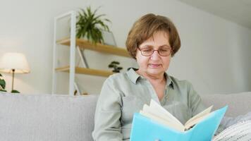 Smiling senior woman relaxing holding book reading sit on sofa at home video