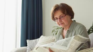 Senior woman with glasses reads newspaper at home video