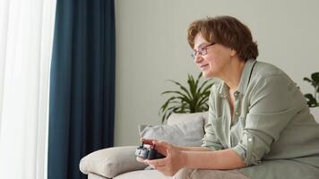 Senior woman gamer sits on the sofa, plays and wins in games on the console. She plays with a wireless controller video