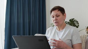 leende äldre mogna kvinna chattar på social nät på Hem. Lycklig äldre pensionär webb surfing information video