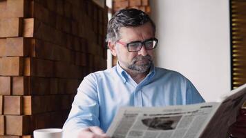 Senior homem lê uma jornal sentado dentro uma acolhedor cafeteria video