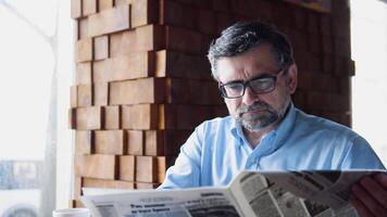 Senior man reads a newspaper sitting in a cozy cafe video