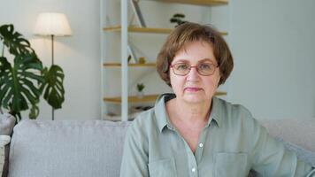 Beautiful senior lady looking in camera sitting in the living room of her house video