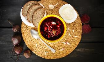 Red traditional russian and Ucrainian borscht or beetroot soup with sour cream, garlic and flavorings in a yellow ceramic cup on wicker placemat background. photo