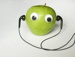 Green small apple with cute eyes and headphones on white background. Conceptual photo. photo