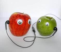 Red and green small apples with cute eyes and headphones on white background. Conceptual photo. photo