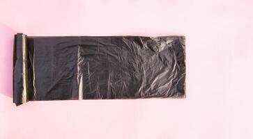 A roll of black plastic garbage bags on pink background photo